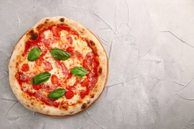 Domuz pastırmalı ve kiraz domatesli pizza ve açık beton ya da taş masada fesleğen..