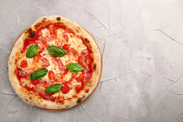 Domuz pastırmalı ve kiraz domatesli pizza ve açık beton ya da taş masada fesleğen..