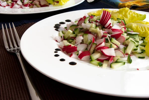 white plate with fresh vegetables: radishes, cucumbers and salad