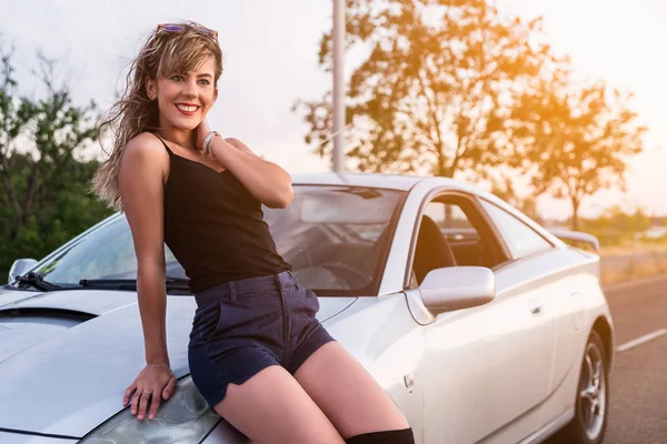 Happy young woman sitting on bonnet of car