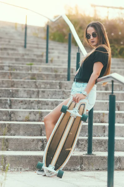 Vacker ung kvinna poserar med en skateboard på sunset — Stockfoto