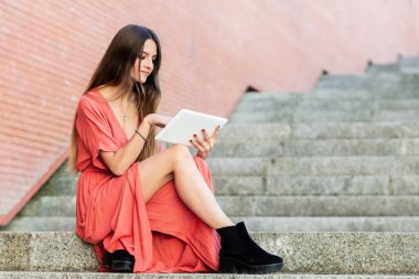Genç, güzel bir kadın merdivenlerde tablet kullanıyor..