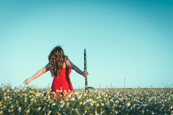 woman in a red dress and a clarinet enjoying freedom in a field of daisies
