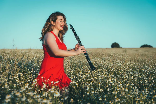 woman in a red dress playing the clarinet in a field of daisies