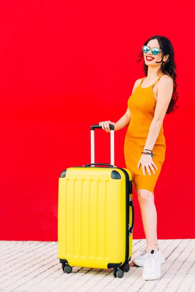 Szczęśliwa kobieta trzyma walizkę i uśmiecha się stojąc Obrazek Stockowy