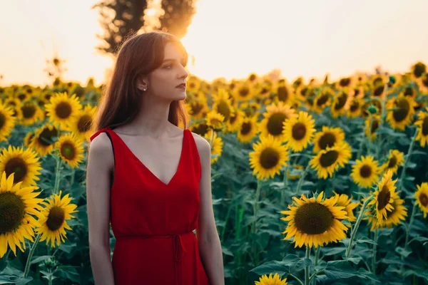 Kvinna med röd klänning i solrosor fält — Stockfoto