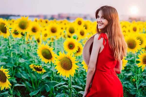 Kvinna med röd klänning och hatt i solrosor fält — Stockfoto