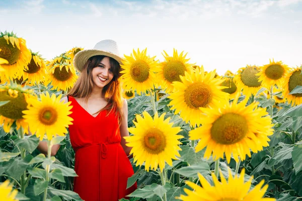 Kvinna med röd klänning och hatt i solrosor fält — Stockfoto
