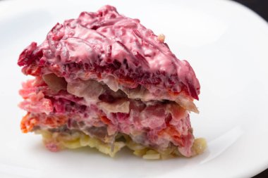 Ringa balığı salatası altında beyaz bir plaka üzerinde bir kürk parçası. Geleneksel Rus katmanlı salatası.