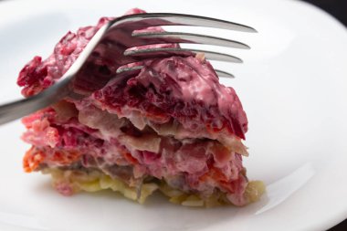 Bir kürk manto altında ringa balığı. Bir çatal ile kesme marul. Geleneksel Rus katmanlı salatası.