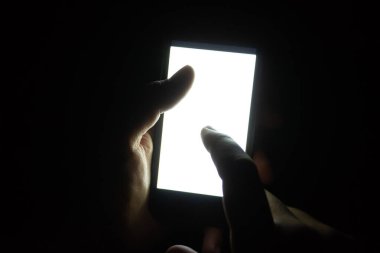 Bir el, karanlıkta boş bir ekranla telefonu tutuyor, bir parmak ekrana dokunuyor..