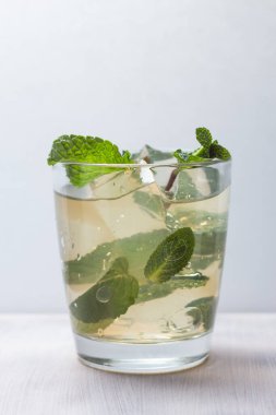 Beyaz arka planda meyve suyu, buz ve nane yapraklarıyla dolu bir bardak. Kokteyl tazeleniyor.