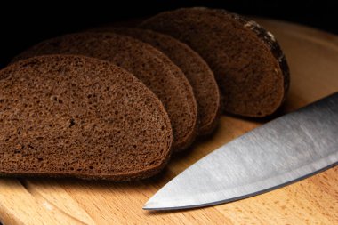 Dilimlenmiş siyah ekmek ve tahta bir tahta üzerinde bıçak.