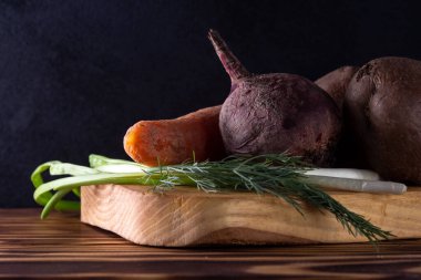 Ahşap bir tahtada kaynamış sebzeler, karanlık bir arka planda, salata malzemeleri.