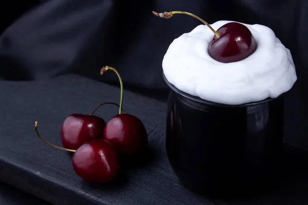 Sweet cherry with cream in  black plastic cup on  burnt wooden board, leather background