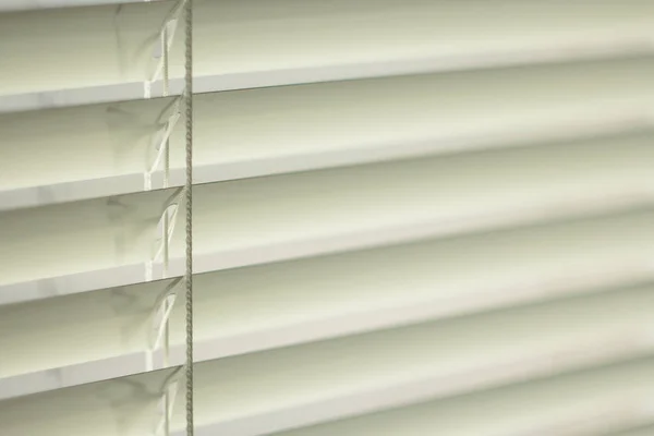 White metal jalousie on the window, daylight passes through the slots of the window blinds