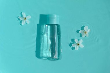 Mavi arka planda su ve çiçekli kozmetik şişesi.