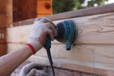 İnşaatçı bir öğütme makinesi tutuyor. Ahşap yüzeylerin temizlenmesi ve parlatılması.