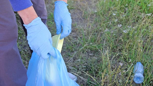 volunteer man collects trash in the forest. collecting waste, clearing the forest of plastic.