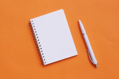 Turuncu arka planda bir defter ve kalem. Üst görünüm, bir yazı için yer.