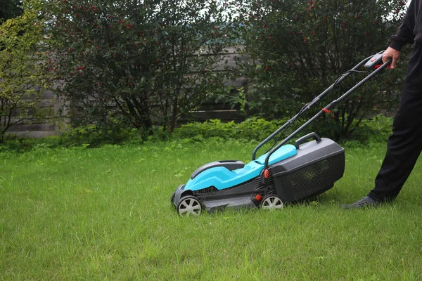 The gardener holds the handle of the lawn mower. Lawn mowing.