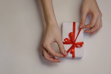 Kadın elleri arka planda kırmızı kurdeleyi bir hediye kutusunda çözer. Noel ve Yeni Yıl veya yeni yıl kutlamaları. Seçici odak