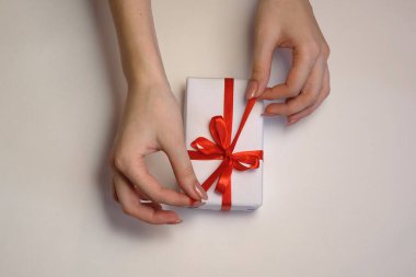 Kadın elleri arka planda kırmızı kurdeleyi bir hediye kutusunda çözer. Noel ve Yeni Yıl veya yeni yıl kutlamaları. Seçici odak