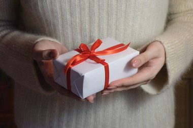 Noel ve Yeni Yıl için içinde beyaz ve kırmızı kurdeleler olan hediye paketi taşıyan bir kadın eli. Seçici odak