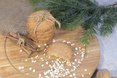 Yuvarlak yulaf ezmeli kurabiyeler, tarçın çubukları ve ahşap bir tahtanın üzerindeki ladin filizi.