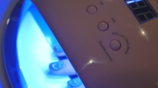 Uma jovem seca as unhas em um salão de beleza em uma máquina especial. Polidores de gel em luz ultravioleta . — Vídeo de Stock