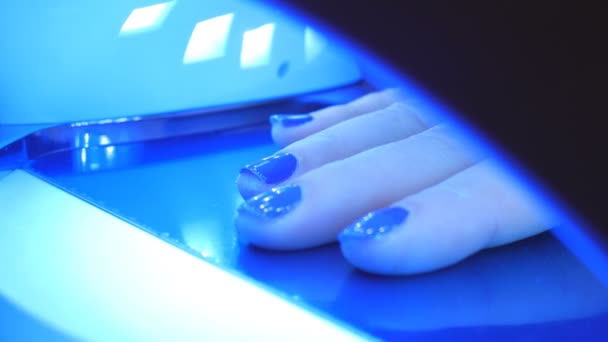 Młoda kobieta wysycha paznokcie w salonie paznokci w specjalnej maszynie. Lakiery żelowe w świetle ultrafioletowym. — Wideo stockowe