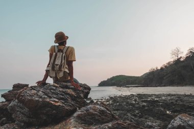 young man with backpack sitting on rock and looking scenery. concept for adventure and travel sea in  summer vacations and outdoor alone