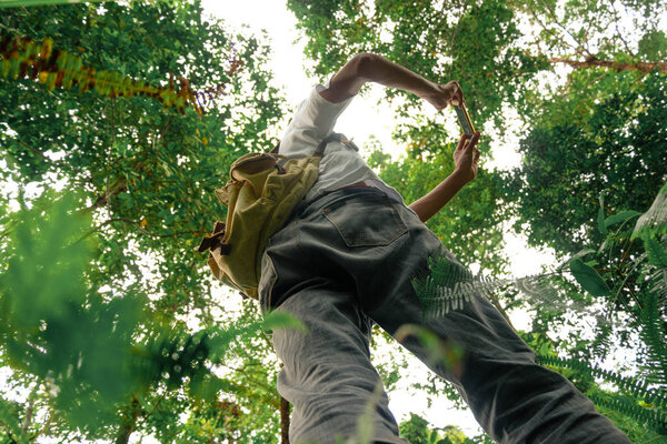 вид снизу на юную авантюристку с рюкзаком, фотографирующим с камерой телефона в лесу. Концепция, уходящая от всего этого
