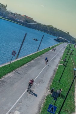Krakow, Polonya-21 Eylül 2019: Insanlar, arka planda Kotlarski Köprüsü ile Vistula nehrinin kıyısında bisiklet yolu üzerinde yürüyüş ve bisiklete binmek