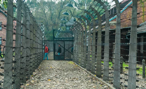 Oswiencim, Polonia - 21 de septiembre de 2019: turistas atravesando una cerca eléctrica con alambre de púas en el campo de concentración nazi de Auschwitz en Oswiecim, Polonia, Patrimonio de la Humanidad por la UNESCO —  Fotos de Stock