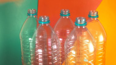 Deniz yeşili, turuncu ve sarı ile renkli canlı bir arka plan üzerinde, hiçbir kapaklar ile 5 boş ve geri dönüşümlü su şişeleri, bir paket. Yeniden Kullanım, Çevre Dostu, Çevre konsepti.