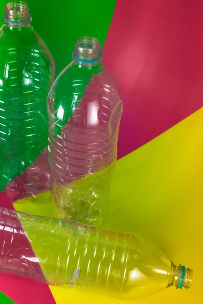 Un pack de 3 bouteilles d'eau vides et recyclables, sans bouchons, sceau bleu, sur un fond vert vif coloré, rouge vin et jaune. Réutilisation, Respectueux de l'environnement, Concept environnement . — Photo