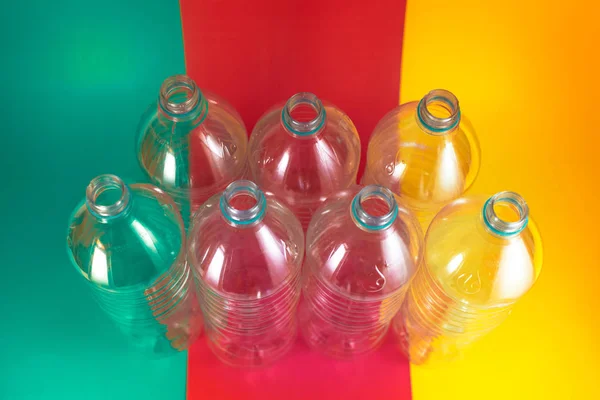 Un pack de 7 bouteilles d'eau en plastique vides et recyclables, sans bouchons, sceau bleu, sur un fond vert de mer coloré, rouge vin et jaune. Réutilisation, respectueux de l'environnement, concept d'environnement. Vue du dessus . — Photo