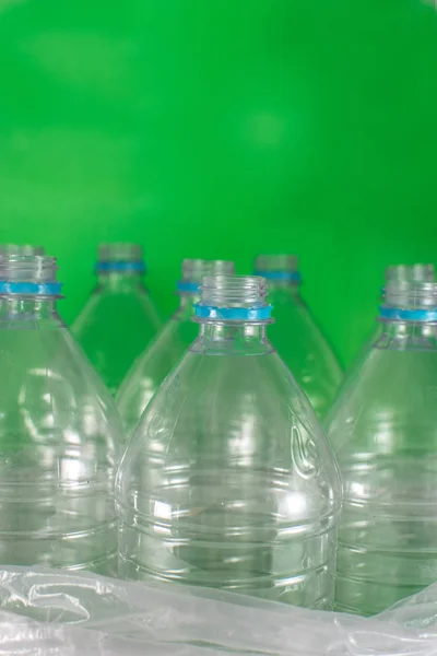 Verticam image of a pack of 8 empty and recyclable plastic water bottles, with no caps, blue seal, in a plastic bag, on a colored  green background. Reuse, Eco-Friendly, Environment concept.