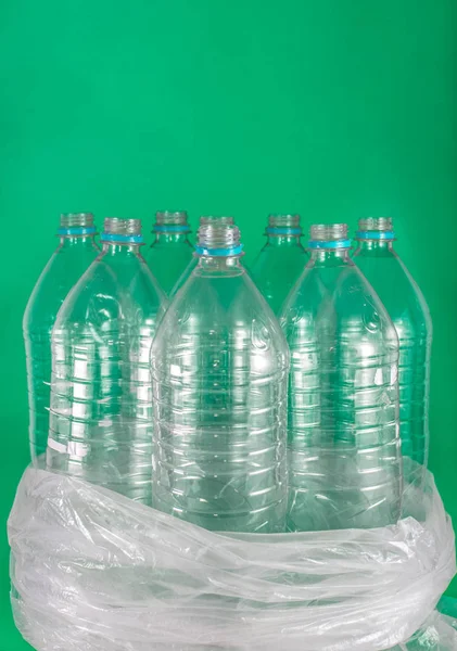 Verticam image of a pack of 8 empty and recyclable plastic water bottles, with no caps, blue seal, in a plastic bag, on a colored  sea green background. Reuse, Eco-Friendly, Environment concept.
