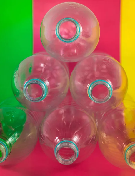 Paquet triangulaire de 6 bouteilles d'eau en plastique vides et recyclables, sans bouchons, sceau bleu, sur un fond vert marin vibrant, rouge vin et jaune. Réutilisation, Respectueux de l'environnement, Environnement — Photo