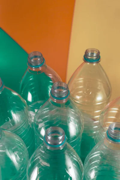 A pack of 8 empty and recyclable plastic water bottles, with no caps, blue seal, in a plastic bag, on a colored pastel tones of sea green, beige and orange background. Reuse, Eco-Friendly, Environment