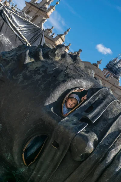 Cracóvia, Polônia - 23 de setembro de 2018: garoto sorridente olhando através do buraco dos olhos da escultura Head Eros Bendato na Market Square, feita pelo artista polonês Igor Mitoraj em Cracóvia — Fotografia de Stock