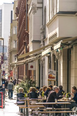 Berlin, Almanya - 26 Eylül 2018: Berlin'in merkezinde bir restoranın masalarında oturan insanlarla işlek bir caddenin kaldırımındaki bazı binaların mimarisinin dikey perspektifi