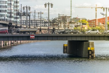 Berlin, Almanya - 26 Eylül 2018: Spree nehri kanalı üzerindeki köprüyü geçen arabalar, kamyonlar ve insanların olduğu yoğun kentsel çevre, reform altındaki binalar ve arka planda kule vinç