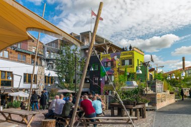 Berlin, Almanya - 26 Eylül 2018: Pampa plaj barında ahşap banklarda oturan ve Spree nehri yakınındaki Holzmarkt'ta bira içerken ürperen bir grup adama renkli bir bakış