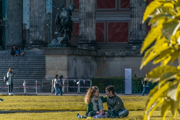 БЕРЛИН, ГЕРМАНИЯ - 28 июля 2018 года: Страстная пара сидит на траве и наслаждается солнечным светом в парке Lustgarten Музейного острова, напротив Музея Альтеса, здания мирового наследия — стоковое фото