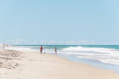 Bahia, Brezilya - 27 Haziran 2019: Porto Seguro'daki yerliler plajında Brezilya'nın kuzeydoğusundaki berrak yeşil okyanus suyunun yakınında sıcak bir yaz gününde topla oynayan iki çocuk