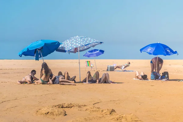 ESPIRITO SANTO, BRAZIL - June 27, 2019: Group of tourists laying in the sand, sunbathing and unders colorful parasols near the cara lagoon at the state park Paulo Cezar Vinha, Setiba — Stock Photo, Image