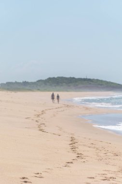 Kumdaki ayak izleri, bitki örtüsüyle kaplı bir tepeye çıkan bir çifte ulaşıyor, yanlarında Setiba, Espirito Santo'daki Paulo Cezar Vinha parkında atlantik ve köpüğü var.